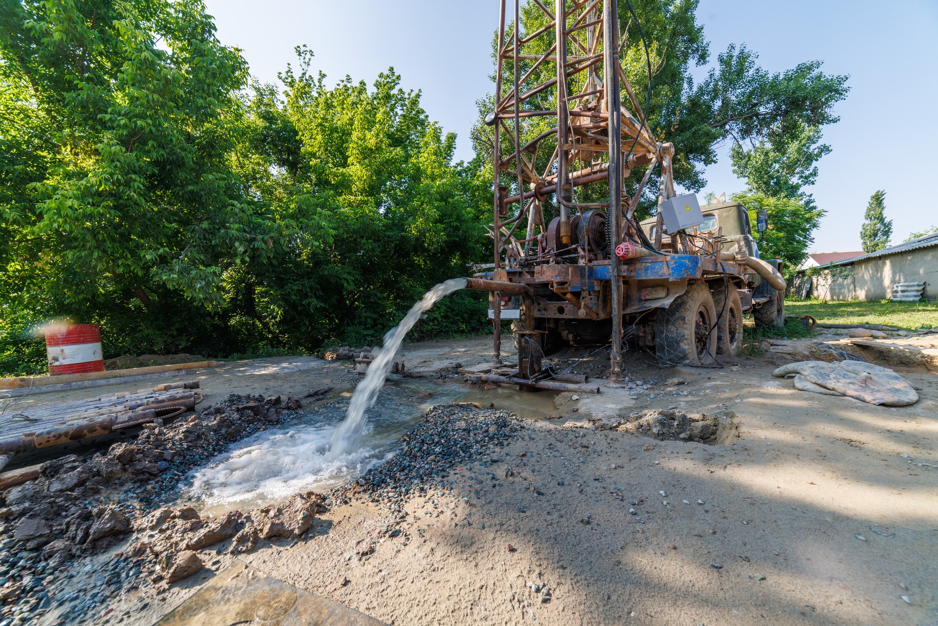 old water pump truck extracts water from a hole in the ground at sunny summer day